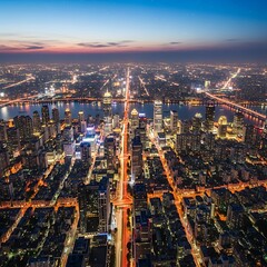 Obraz premium A vibrant cityscape glows at twilight, showcasing a network of illuminated roads and towering buildings, stretching across a wide river valley.