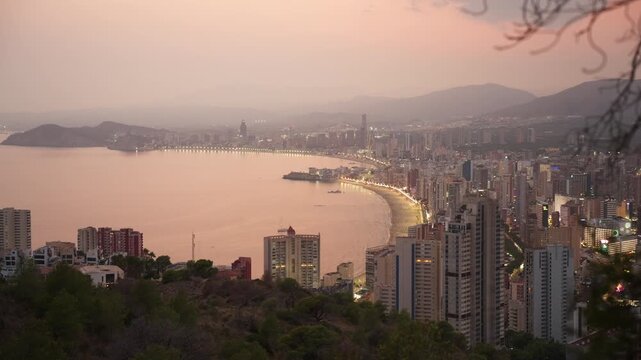 Overhead view of benidorm at sunset, skyscrapers and illuminated shoreline glowing along the costa blanca as twilight paints the mediterranean sky over the beach and bay