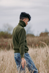 A solitary subject walks through tall meadow grass, dressed in a textured green knit turtleneck and...