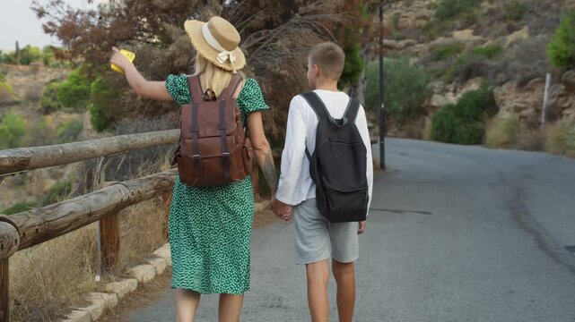 Back view of caring mother holding hands with son as they stroll along scenic country lane, embracing their close relationship and shared passion for outdoor adventures - Powered by Adobe