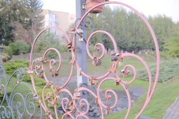 Many locks are attached to a pink heart shaped railing on a bridge.