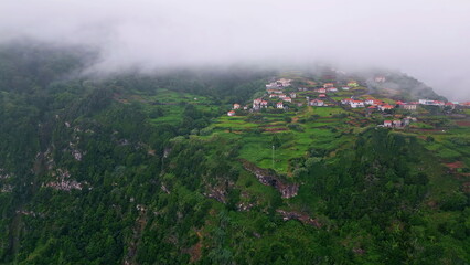 Foggy mountains village drone view. Rural community green fields with low clouds
