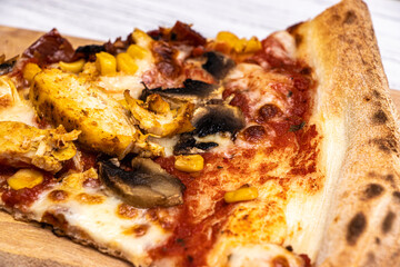 Close-up of a delicious slice of pizza topped with chicken, corn, and mushrooms, presented on a wooden board against a light background, perfect for food enthusiasts and restaurateurs.