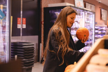 Business smiling long hair woman examining a pumpkin in the produce section of a supermarket....