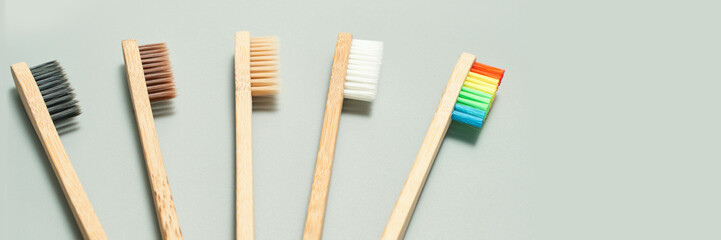 Bamboo toothbrushes with multicolored bristles on gray background for eco-friendly oral care.