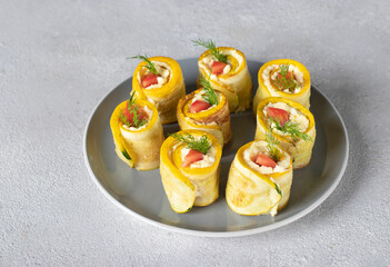 Zucchini rolls with garlic, cream cheese and tomato on gray plate