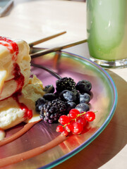 Close up of fluffy pancakes with strawberry sauce and mixed berries in bright daylight with matcha beverage