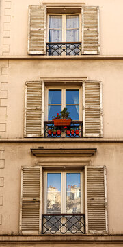 Paris apartment building showing classic balconies, windows with open shutters, and flower pots. Paris, France