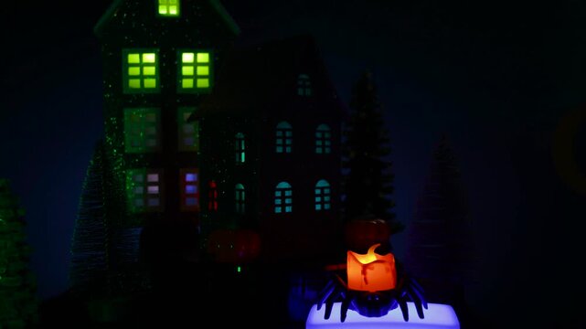 Amidst the flashing lights, an atmospheric Halloween town features a revolving house surrounded by glowing pumpkins and a candle and candle in a spider's candlestick in the foreground