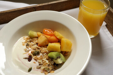 Serving a healthy breakfast of yogurt, granola, fruit, and orange juice on a wooden tray. Cotswolds countryside, England