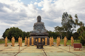 The main stone Buddha statue seated on a pedestal, surrounded by a ring of standing golden figures,...