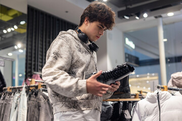 Teen boy shopping for shoes in clothing store — young man holding black boots, teenage fashion,...