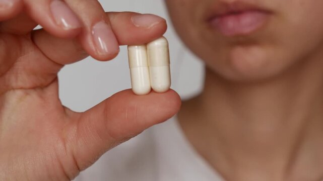 Two white capsules in woman's hand &ndash; daily vitamin intake for immune support.