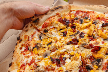 Delicious pizza topped with chicken, sun-dried tomatoes, corn, and mushrooms being held by a persons hand. Perfect for takeout or delivery meal ideas.