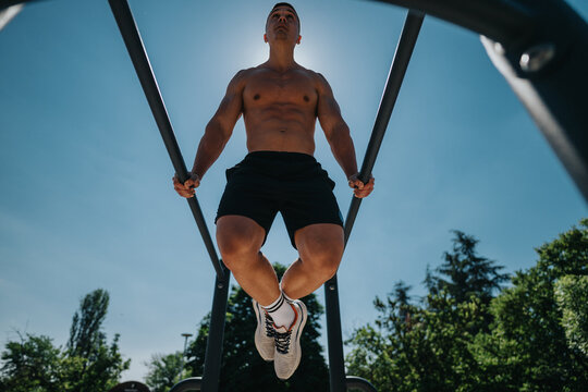 Fit individual performing a calisthenic workout using parallel bars in a green park setting on a bright sunny day, demonstrating strength, balance, and determination.