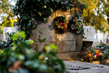 Old grave covered with ivy and floral wreaths in soft evening light