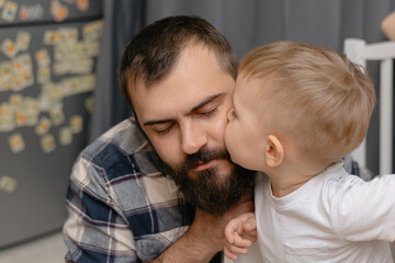 Tender moment: caucasian male toddler kisses bearded adult male father in home setting