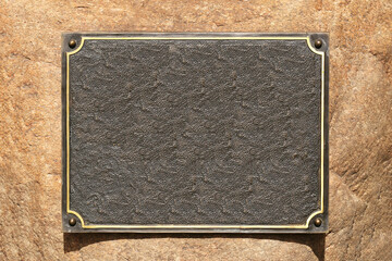 Empty metal plaque on stone wall background. Blank bronze signboard ready for engraving or inscription. Template for memorial plate, name tag, or information sign.