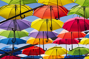 Colorful umbrellas hanging above city street forming bright rainbow canopy. Urban outdoor art installation creating festive atmosphere of happiness, summer joy, diversity and celebration.
