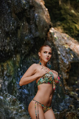 Obraz premium Woman in a tropical print bikini under a waterfall in a rocky jungle grotto