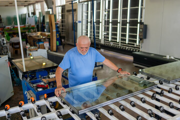 An elderly worker controls the process of installing glass in PVC frames.