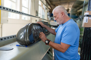 An elderly worker controls the process of installing glass in PVC frames.