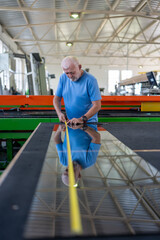 An elderly worker controls the process of installing glass in PVC frames.