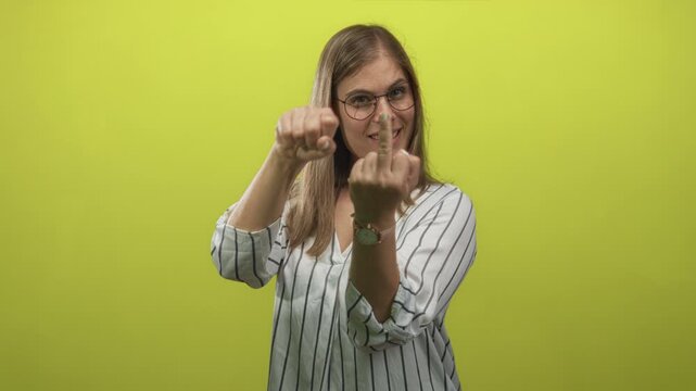 Young blonde woman with glasses shows middle finger and mimics turning a crank in a lime green studio; defiance.