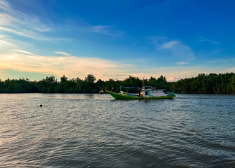 A vibrant green fishing boat floating on a tropical river with a warm sunset sky and palm trees in the background, capturing natural beauty and local culture.