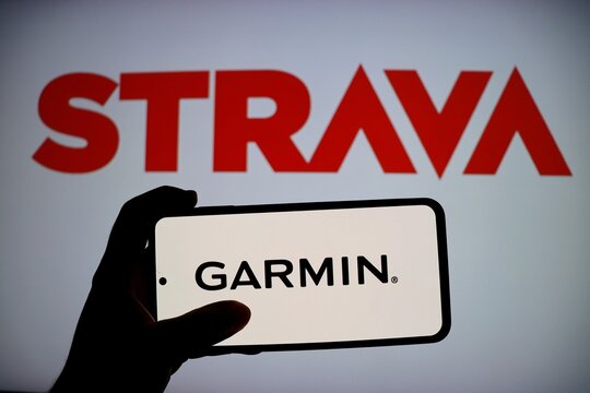 Salvador, Brazil - October 17, 2025: Garmin app on smartphone screen with Strava logo in the background. Strava and Garmin apps. 