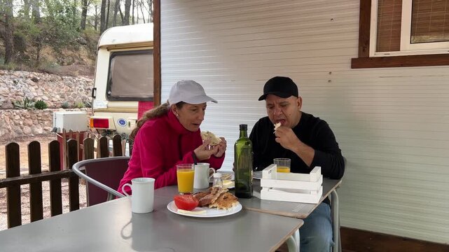 Pareja desayunando frente a su caravana, plano medio, 4K
