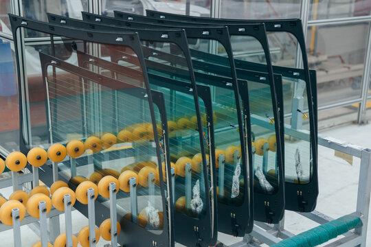 Automotive windshields staged on a production line, mounted vertically in protective yellow racks.