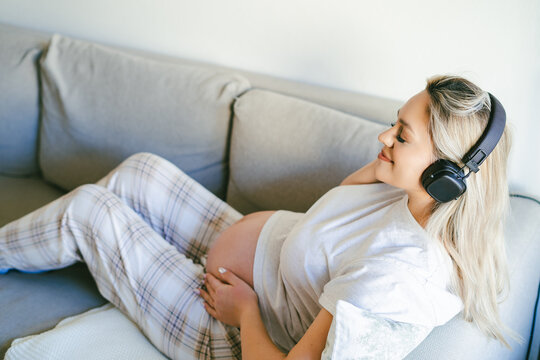 Young happy pregnant woman listening to music for baby in headphones. Motherhood.