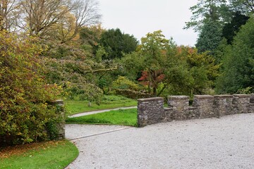 Fototapeta premium Stone wall entrance to green park. Gravel path and grass lead to autumn-colored trees in Sizergh - Kendal - Lake District - UK