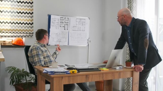 client and contractor finalize plans at desk with floorplans on board, seated professional points at layout while manager leans forward, decisive closeout meeting with documents and measuring tape