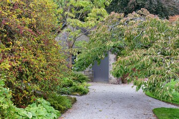 A gravel path leads to a stone building, framed by trees. Lush greenery lines the walkway, creating a serene outdoor setting in Sizergh - Kendal - Lake District - UK