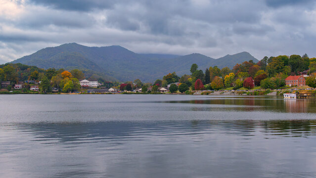 Lake Junaluska, North Carolina, USA | Houses line the quiet lakeshore under gray skies, autumn trees reflecting softly on the still water beneath the Smoky Mountain foothills.