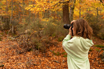 Woman photographing autumn forest landscape with camera