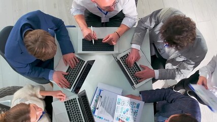 team collaborating over colorful charts, energetic group working together at laptopfilled table, collaborative team engaged in lively brainstorming around triangular table with laptops and colorful