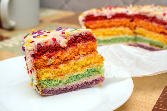 Slice of colorful rainbow cake with white frosting and sprinkles