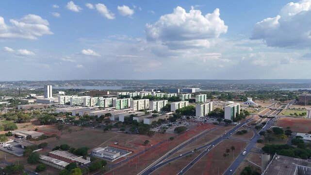 Vista a&eacute;rea ampla dos blocos ministeriais na Esplanada, cercados por vias largas, &aacute;reas abertas e paisagem urbana caracter&iacute;stica de Bras&iacute;lia DF