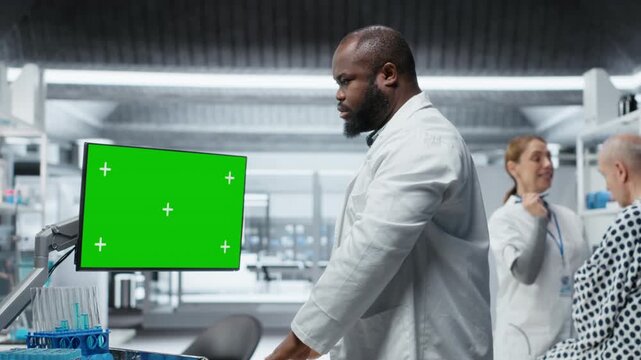 Green screen next to black medic studying data for drug testing in lab, evaluating dosage and potential side effects. Checking chemical reactions and safety to support science breakthrough. Camera B.