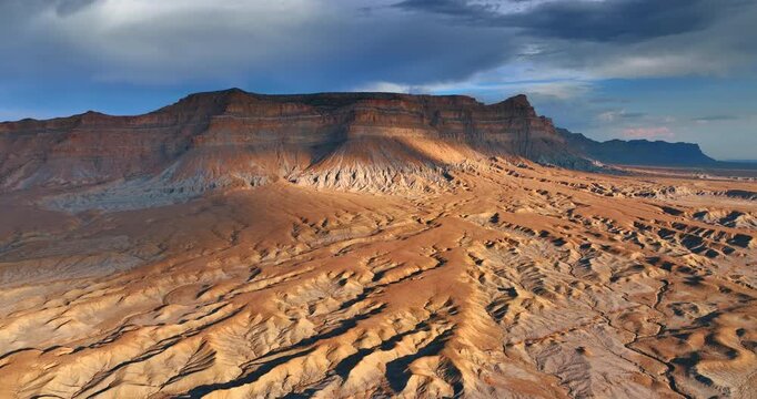 Drone aerial view of a dramatic mesa and eroded desert landscape in Utah during golden hour sunlight.