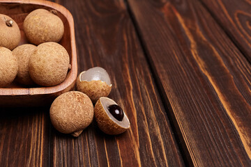 Longan tropical fruit displayed in a wooden bowl on a rustic wooden surface, showcasing its round shape, textured skin, and glossy dark seed, representing exotic flavors and natural beauty