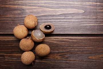 Longan tropical fruit displayed on wooden surface, showcasing its unique texture and color, with one fruit cut open revealing translucent flesh and dark seed, emphasizing natural beauty