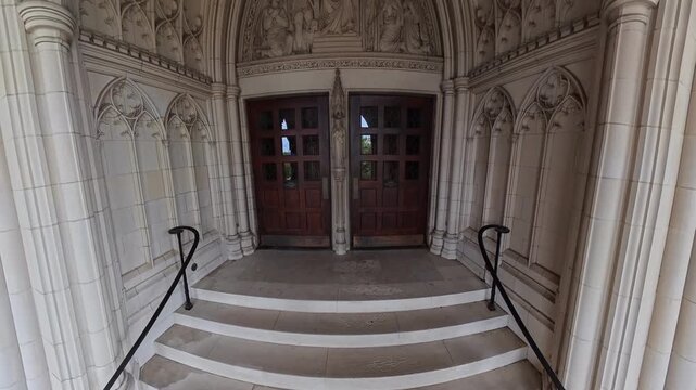 Gothic cathedral entrance with intricate stone carvings, Washington National Cathedral front door detail. video camera pans upward.
