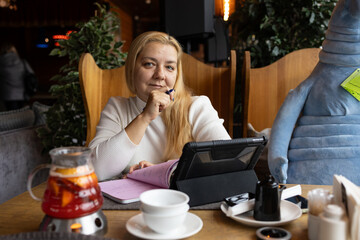 woman writes in a notebook at a cosy café table. A tablet and a cup are nearby, Remote work.