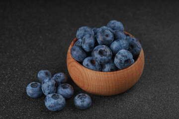 Fresh ripe blueberries in small wooden bowl on dark gray textured stone background. Delicious organic fruit rich in vitamins, wild berries,healthy lifestyle, natural food. Close up, macro