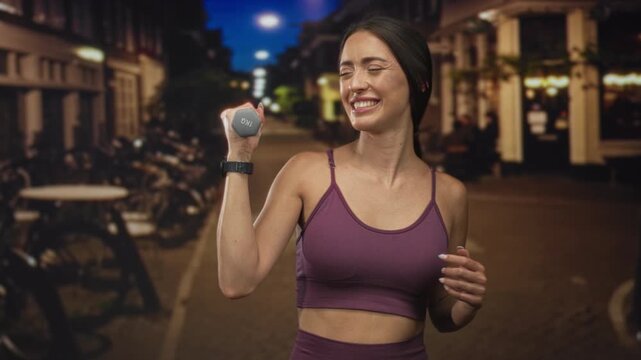 Woman lifting 1kg dumbbell with wristwatch visible on street at night in purple sports top and leggings; urban fitness joy.