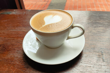 A white coffee cup with a heart drawn on it sits on a wooden table